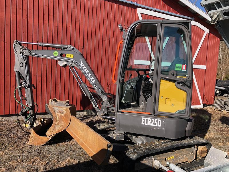Volvo ECR25D minigraver med graveskuff, parkert ved en rød låvevegg